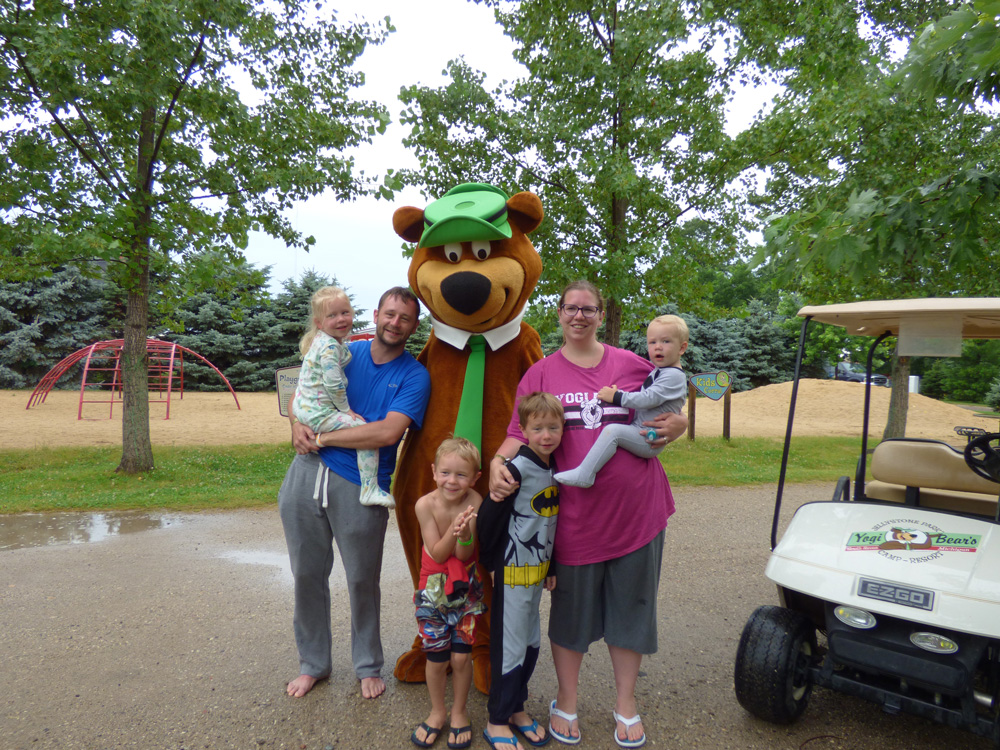Family posing with Yogi Bear™ near a golf cart at Jellystone Park™ South Haven